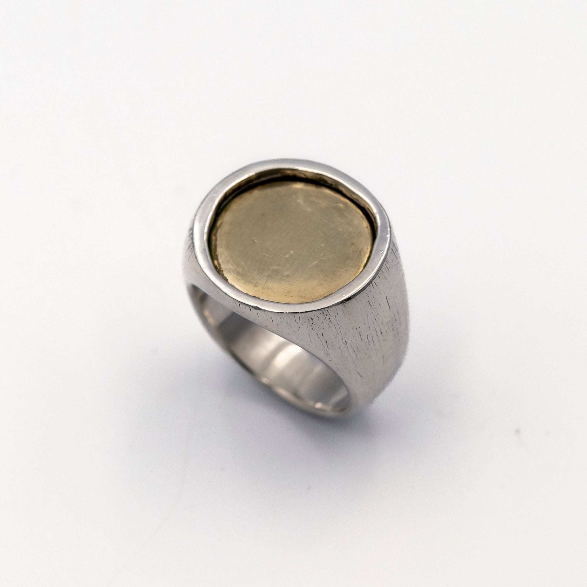 Silver ring with a gold coin inlay on a white background