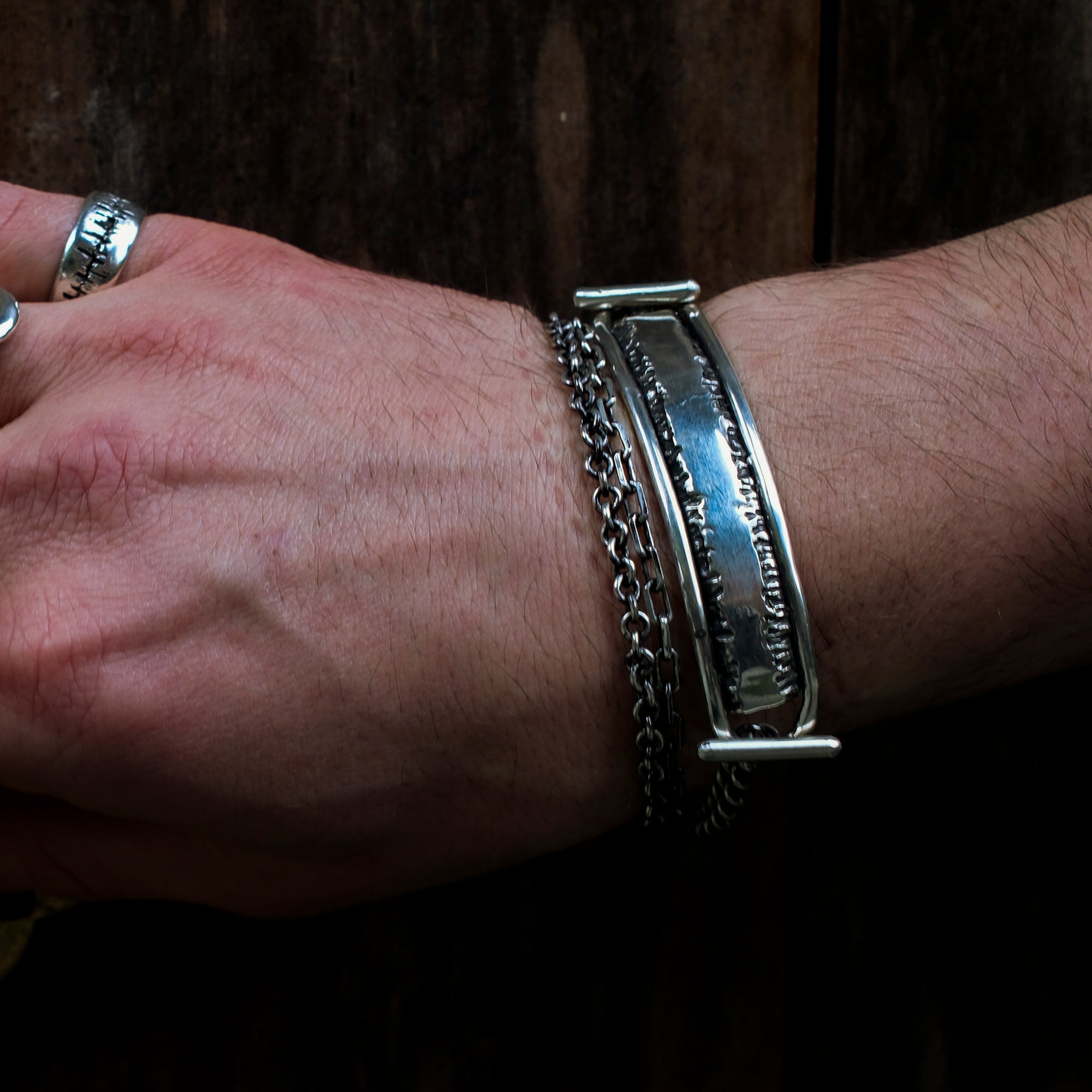 Close-up of a wrist wearing two silver bracelets on a dark background
