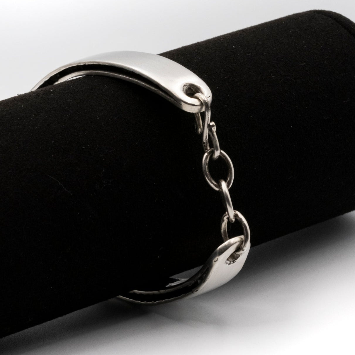 Silver chain bracelet on a black cylindrical object against a white background