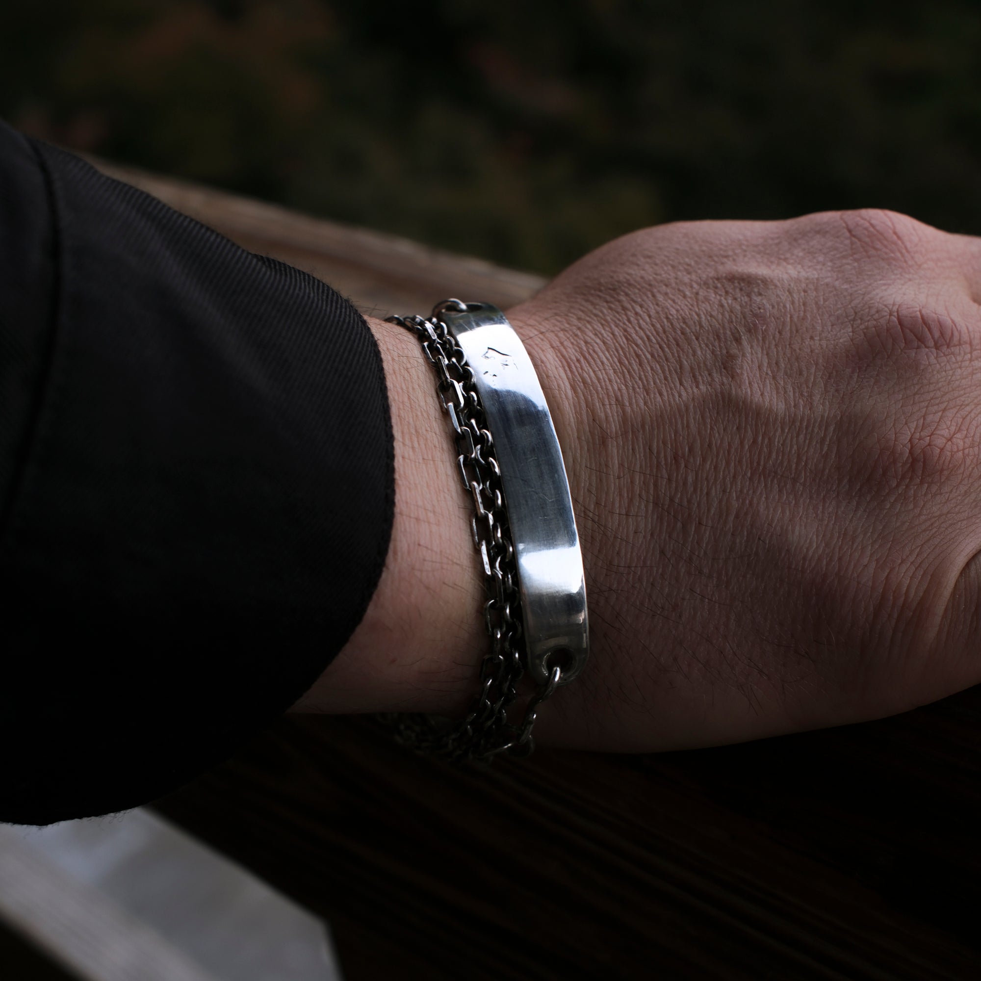 Close-up of a wrist wearing two silver bracelets on a dark background