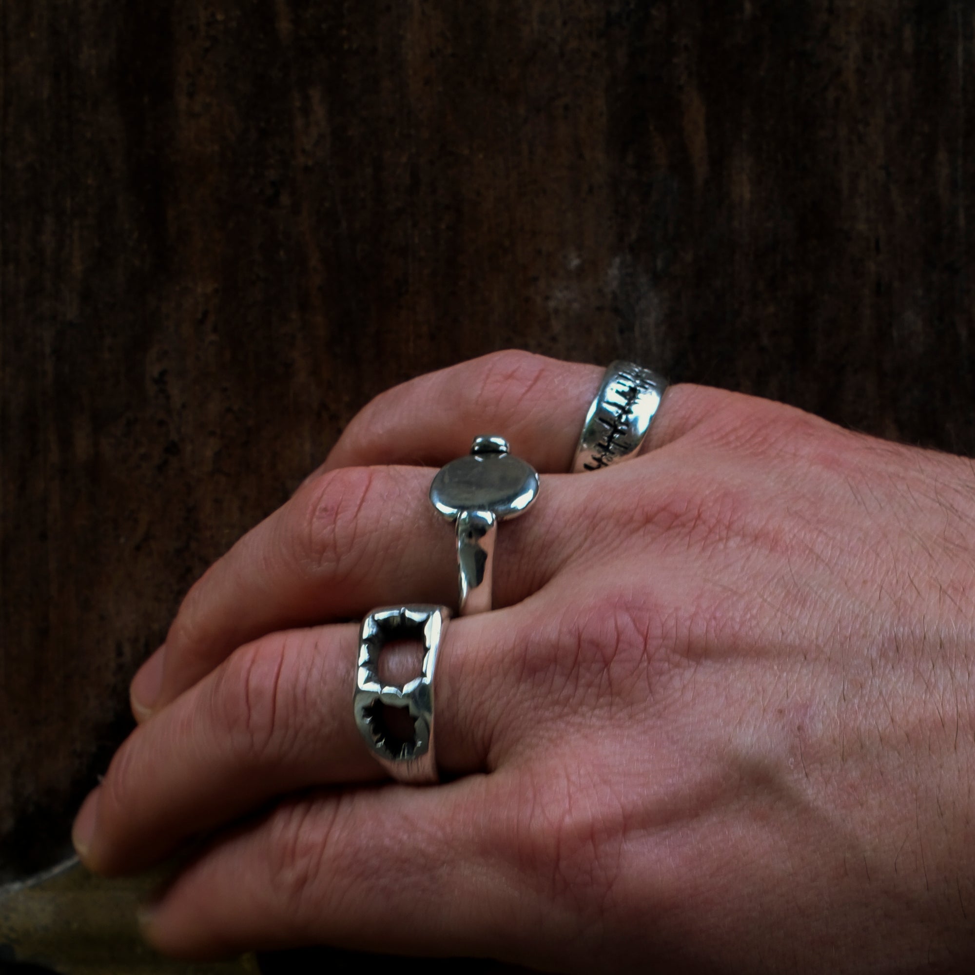 Hand wearing three silver rings with a dark background